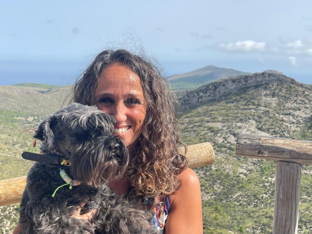 Esther Fuster sonríe con su perro en un paisaje montañoso