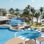 Vista panorámica de un hotel frente al mar con piscina y palmeras