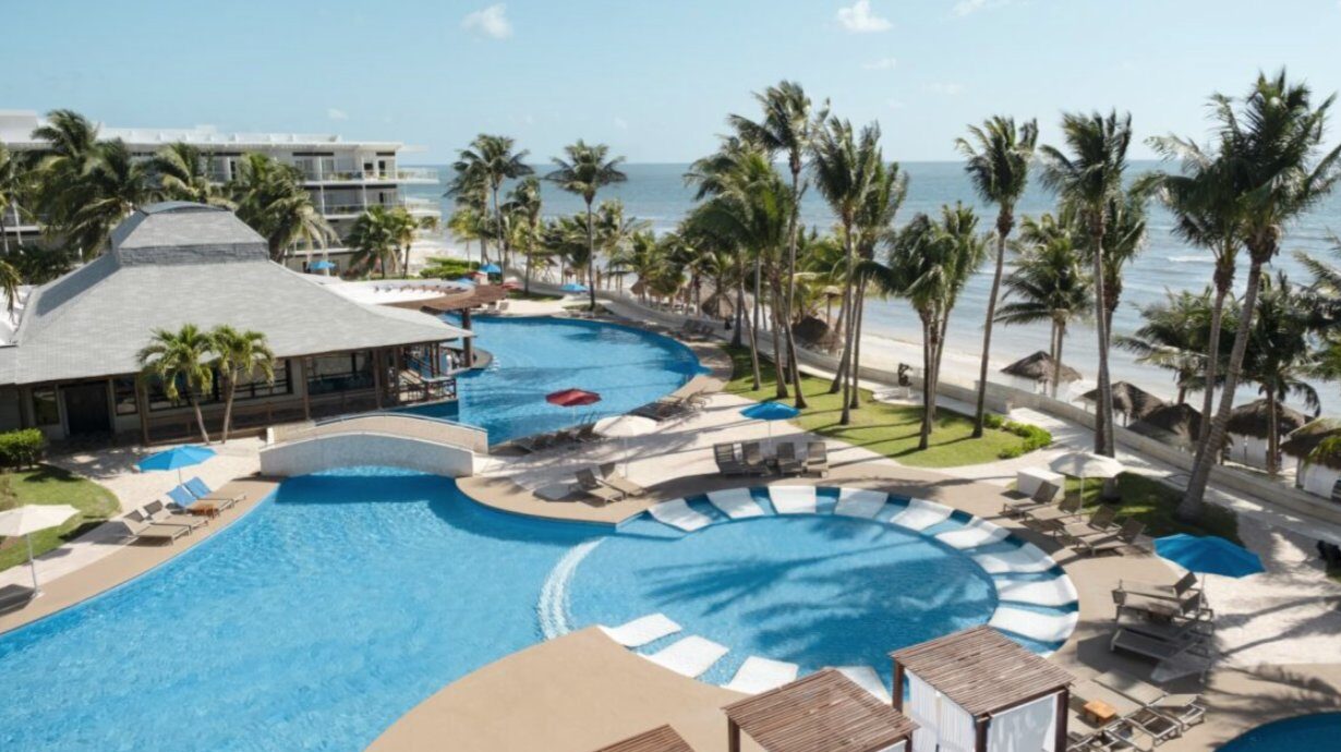 Vista panorámica de un hotel frente al mar con piscina y palmeras