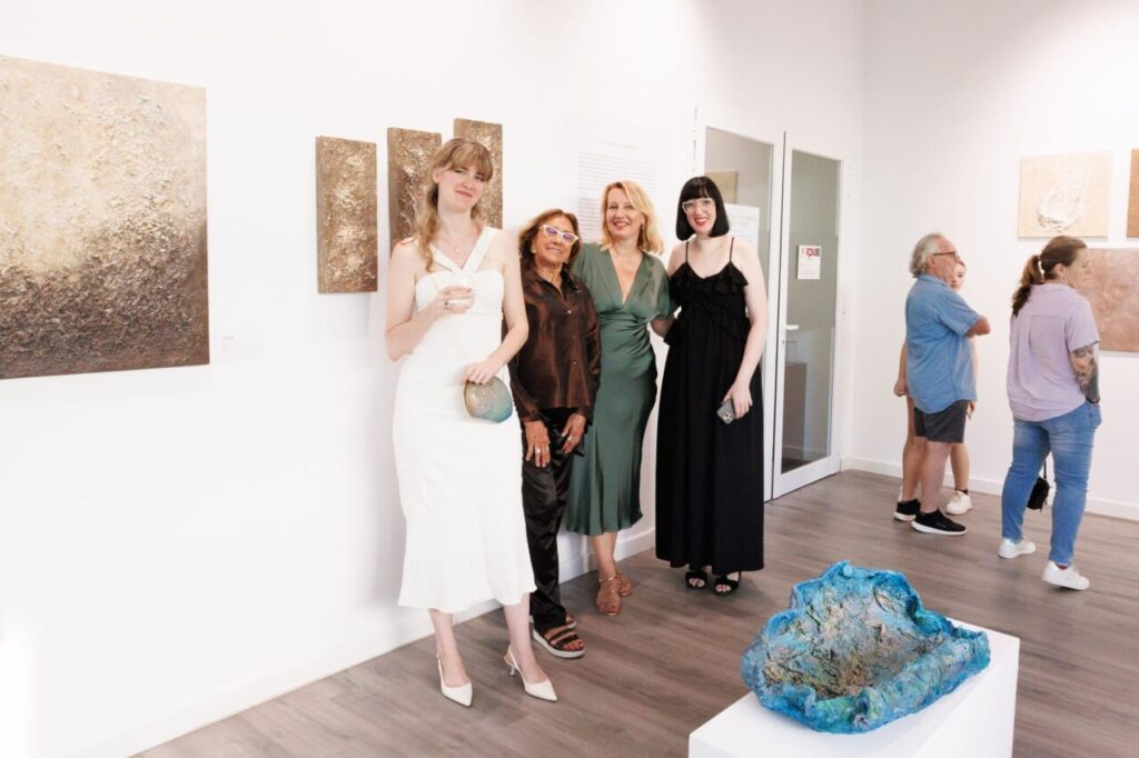 Cuatro mujeres posando en una galer&iacute;a de arte con obras en la pared.