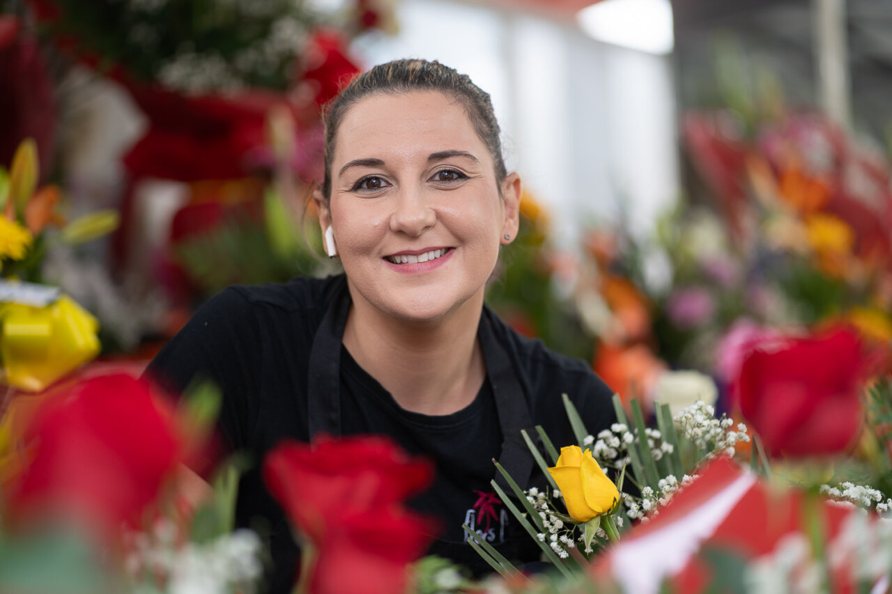 Mujer sonriente rodeada de flores coloridas en un mercado