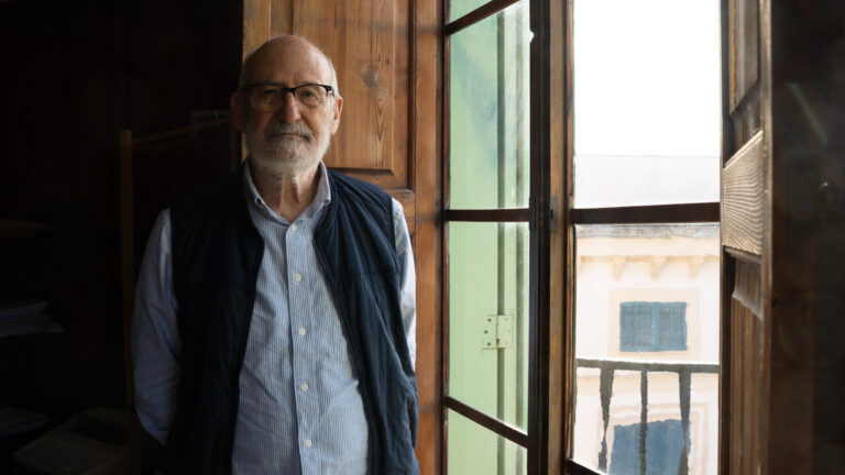 Hombre mayor de pie junto a una ventana en un edificio antiguo