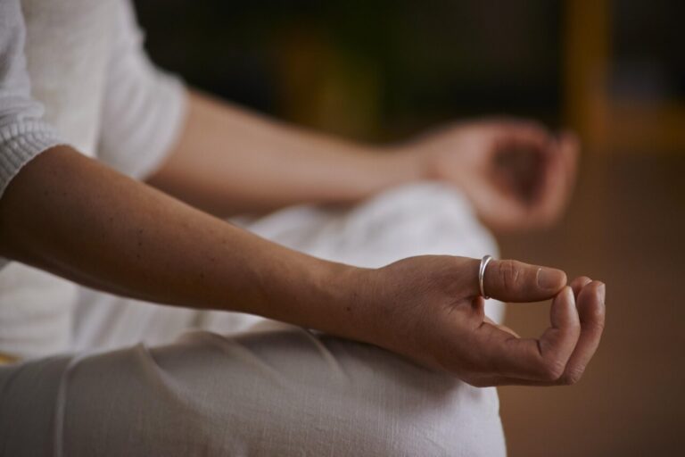 Mano en posición de meditación con anillo en un entorno tranquilo.