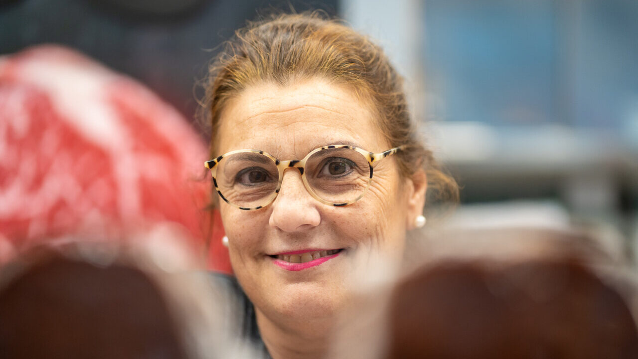 Mujer sonriendo en un mercado con productos de carne al fondo
