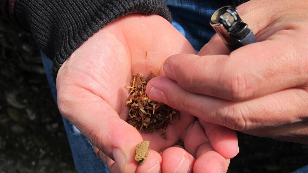 Manos sosteniendo tabaco y un encendedor en un contexto de prevención de adicciones.