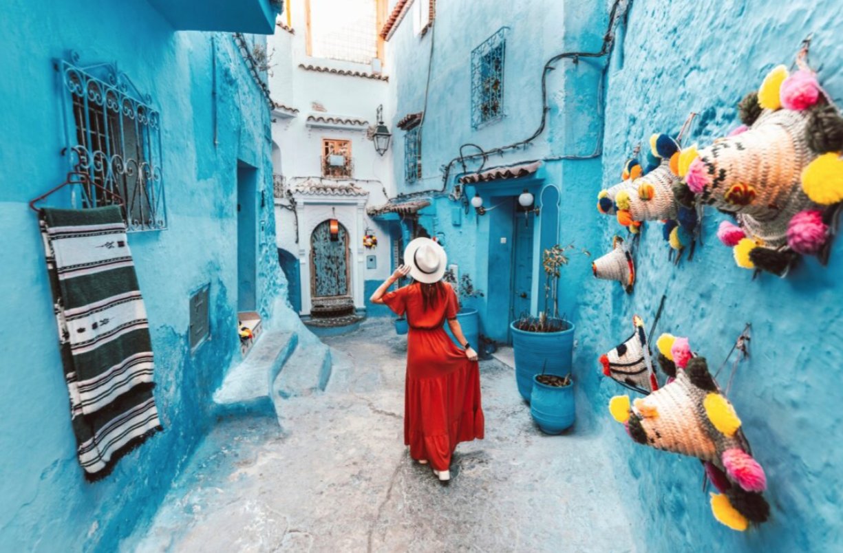 Mujer con vestido rojo paseando por callejón azul en Chefchaouen