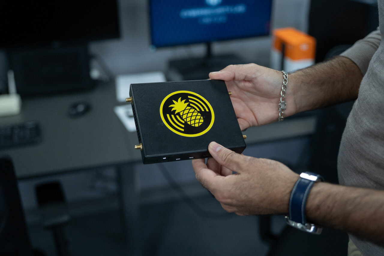 Persona sosteniendo un dispositivo de ciberseguridad con un logo de pi&ntilde;a.