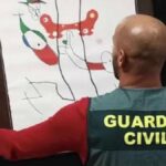 Un agente de la Guardia Civil sostiene una obra de arte recuperada.