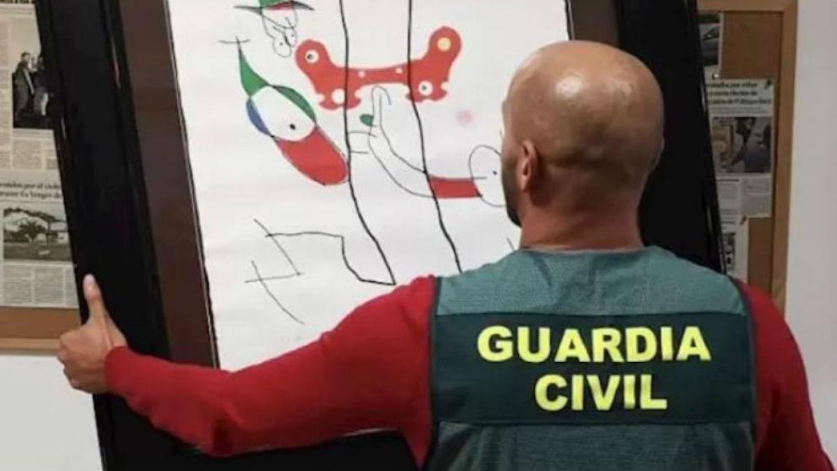Un agente de la Guardia Civil sostiene una obra de arte recuperada.