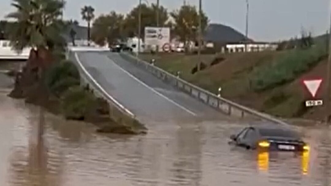 Inundación en carretera con un coche parcialmente sumergido por la lluvia