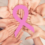Manos unidas sosteniendo un lazo rosa en apoyo al cáncer de mama