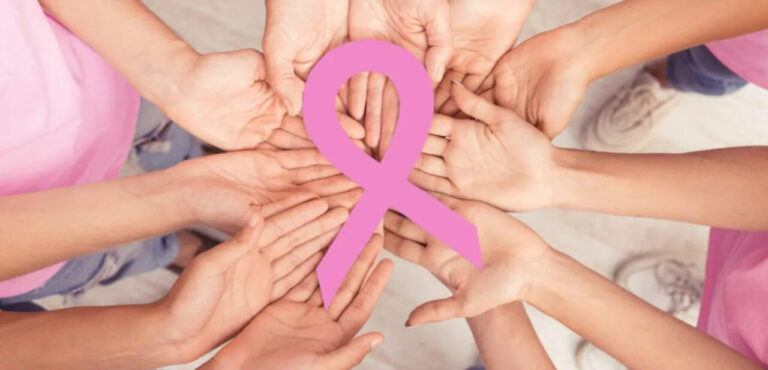 Manos unidas sosteniendo un lazo rosa en apoyo al cáncer de mama