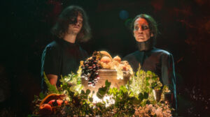 Actores en escena con frutas y vegetación en un espectáculo poético