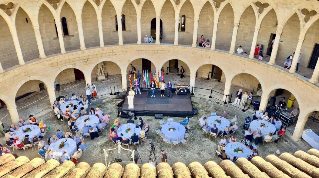Vista del encuentro de casas regionales en el Castell de Bellver con mesas y participantes.