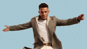 Alejandro Sanz en una pose dinámica con fondo azul.