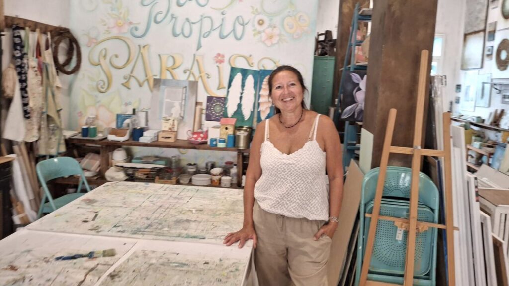 Karina Cappato sonríe en su taller artístico lleno de materiales.