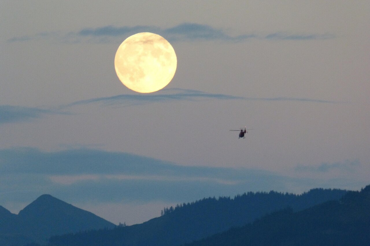 Helicóptero volando bajo una luna llena sobre montañas