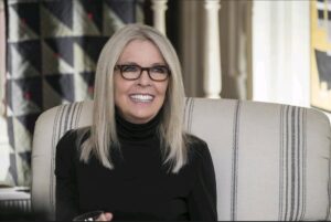 Diane Keaton sonriendo mientras está sentada en un sillón