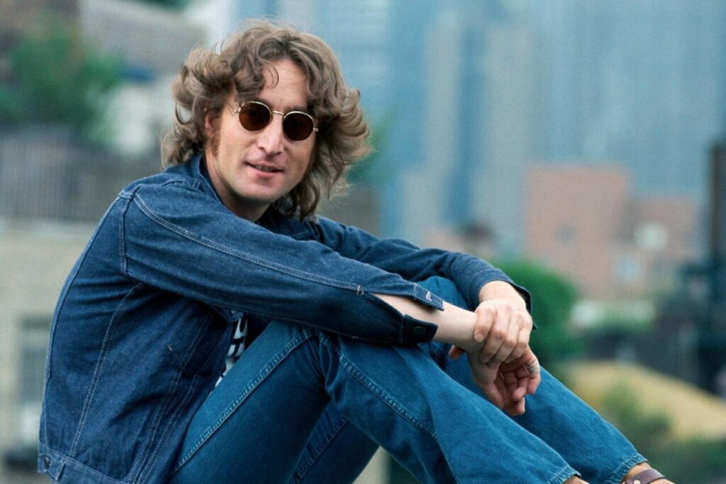 John Lennon sentado con gafas de sol y chaqueta de mezclilla