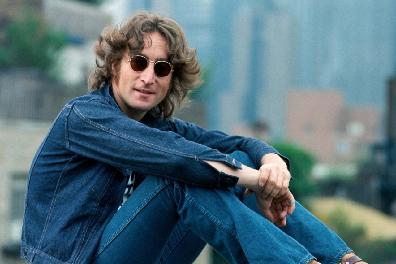 John Lennon sentado con gafas de sol y chaqueta de mezclilla