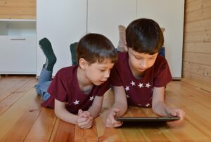 Dos niños usando una tablet en el suelo de madera