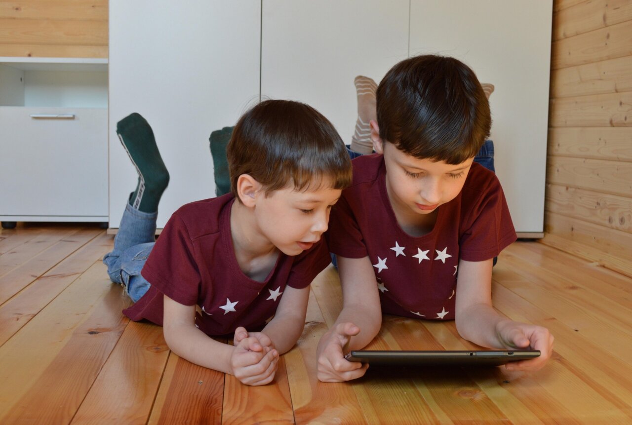 Dos niños usando una tablet en el suelo de madera