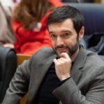 Persona pensativa en un entorno político, con atención en la reunión.