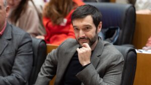 Persona pensativa en un entorno político, con atención en la reunión.