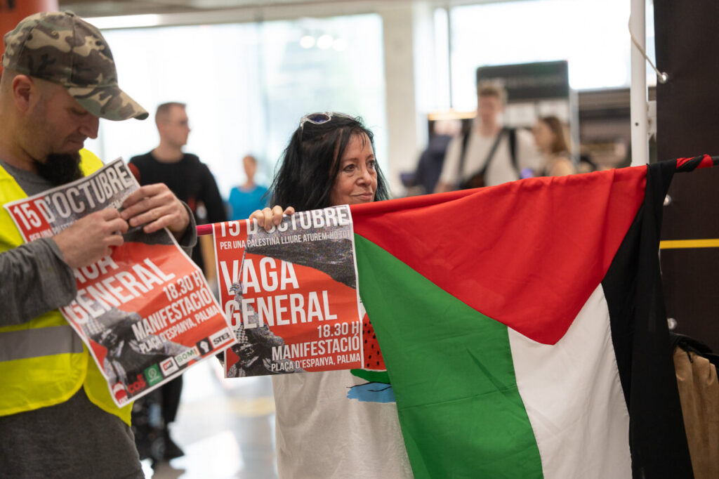 Manifestantes sosteniendo pancartas y una bandera en el aeropuerto