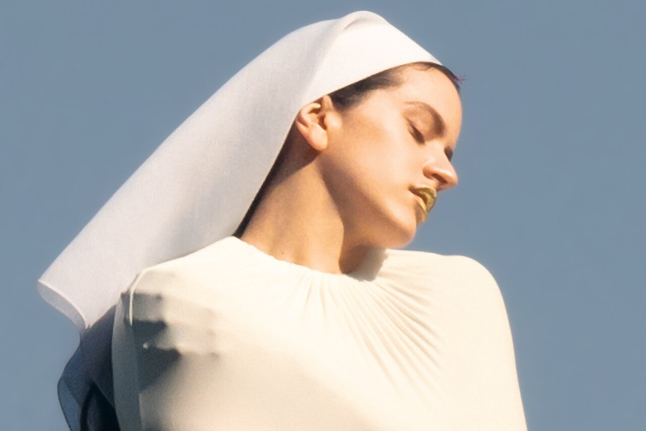 Rosalía en un atuendo blanco con un tocado, mostrando una expresión artística.