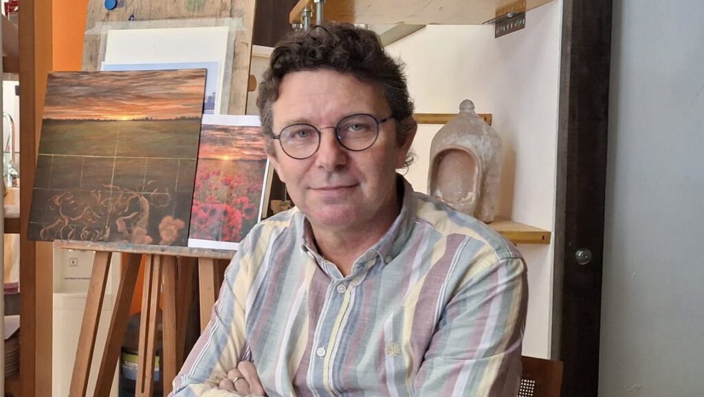 David Santos posando en su estudio de pintura con obras de fondo