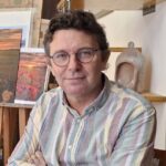 David Santos posando en su estudio de pintura con obras de fondo