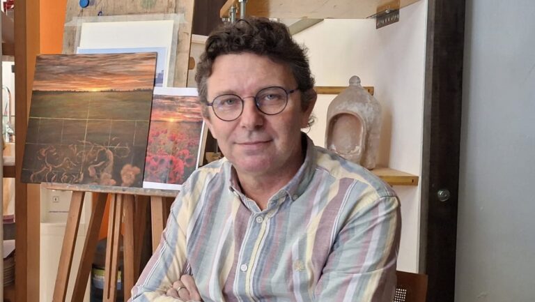 David Santos posando en su estudio de pintura con obras de fondo