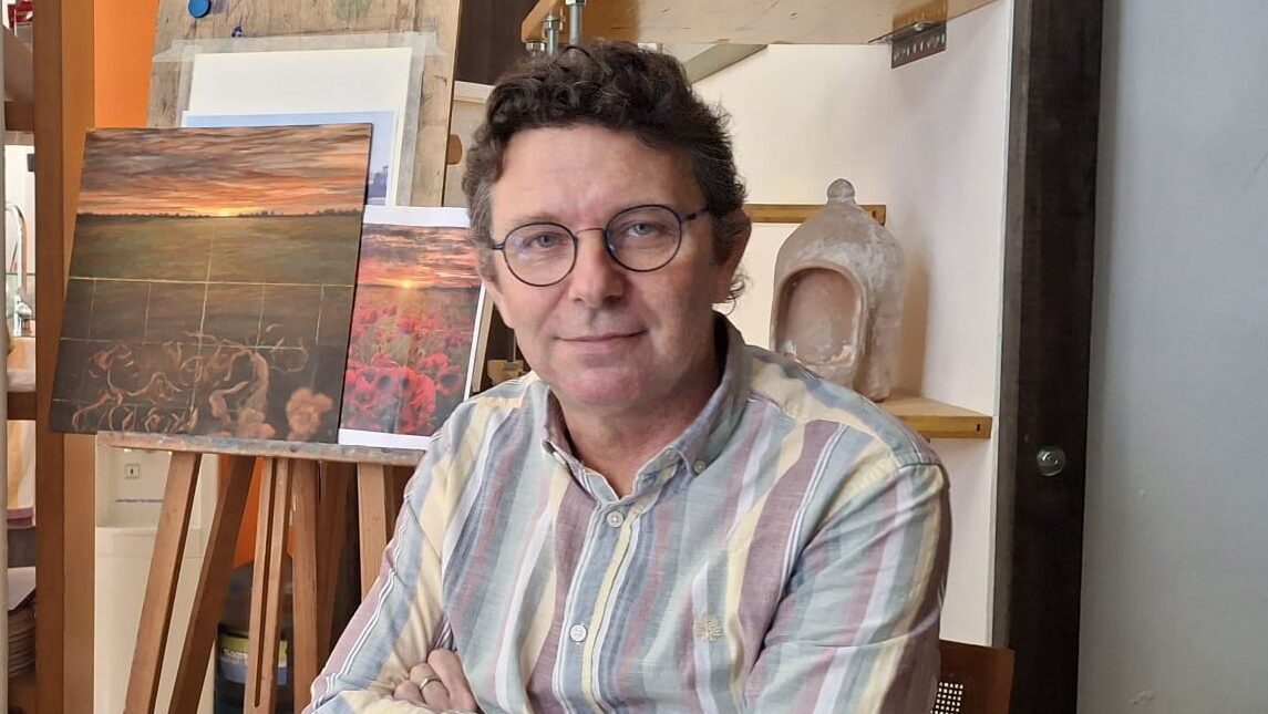 David Santos posando en su estudio de pintura con obras de fondo