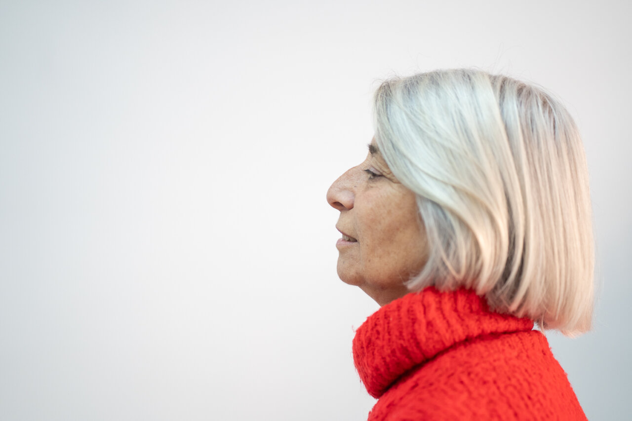 Perfil de mujer con cabello canoso y suéter rojo