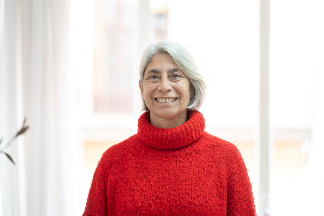 Paz Alcoverro sonriendo con un suéter rojo en un entorno luminoso