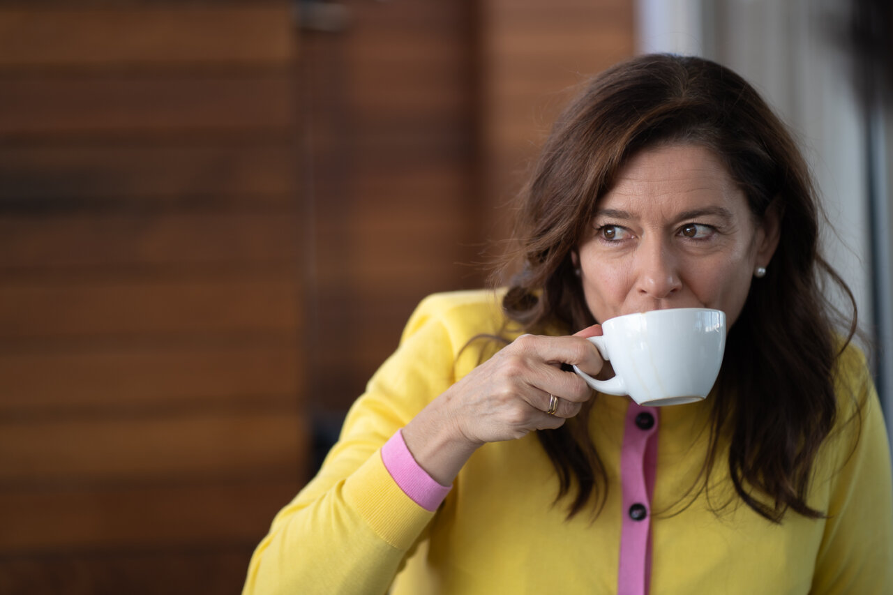 Miriam González tomando café en una terraza con fondo de madera.
