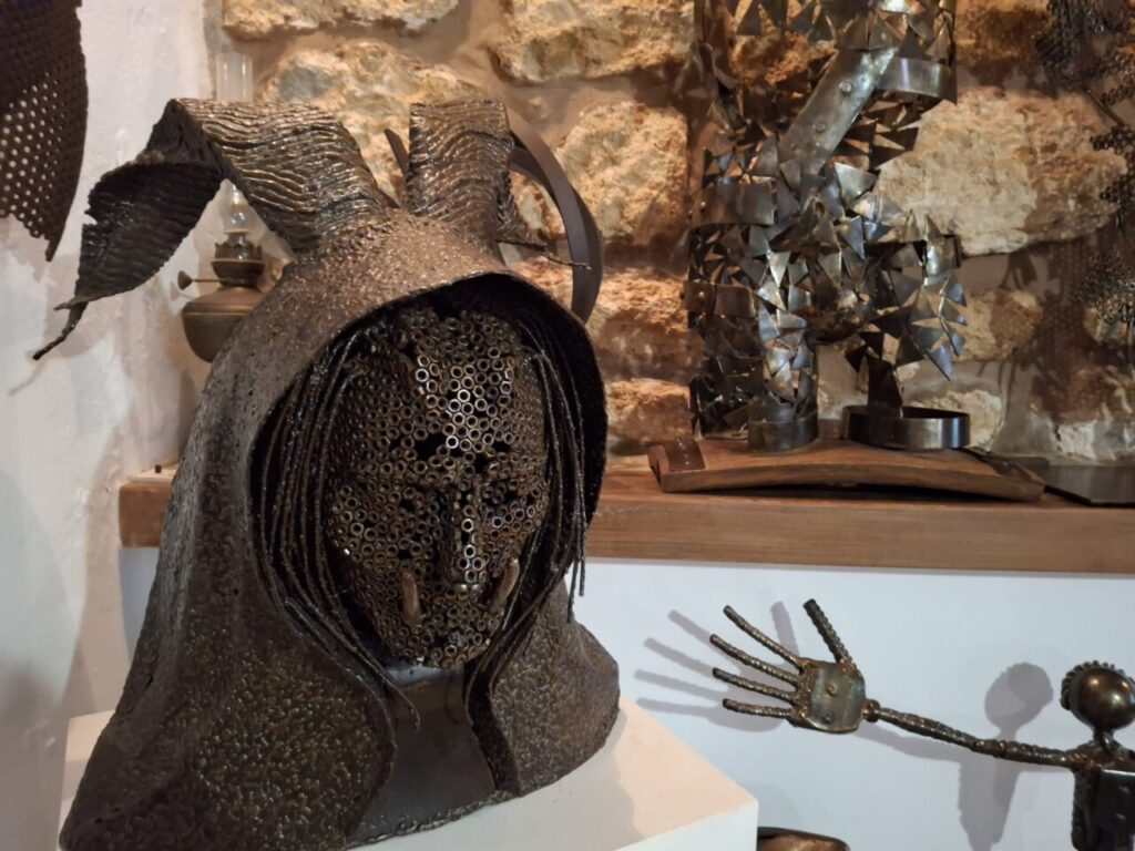 Escultura de metal con rostro humano y orejas en un fondo de piedra.