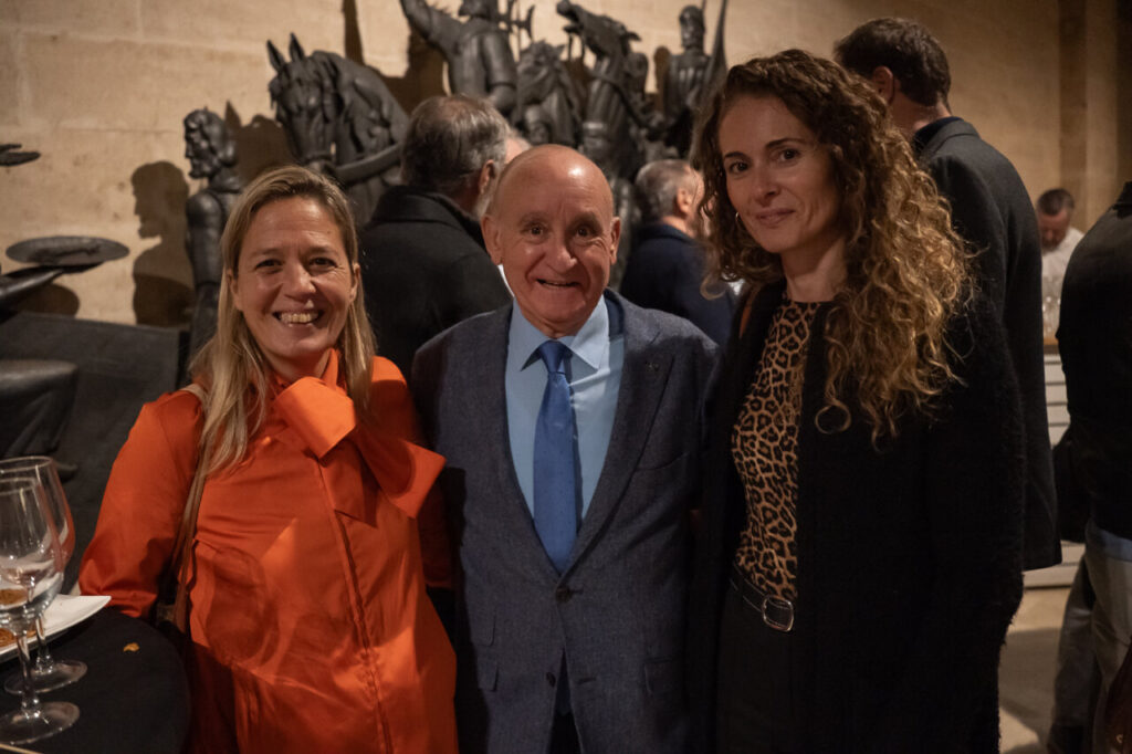 Tres personas sonriendo en un evento social con esculturas al fondo.