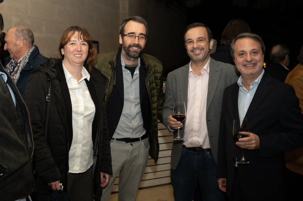 Cuatro personas posando en un evento social con copas de vino