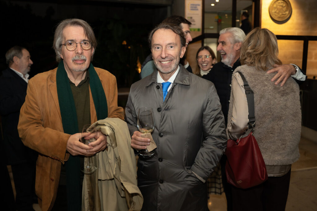 Dos hombres en un evento social sosteniendo copas de vino.