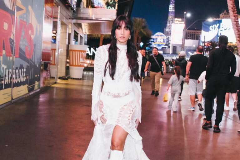 Aitana caminando en una calle iluminada de noche con un vestido blanco