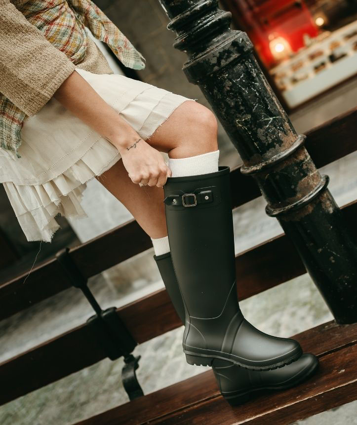 Mujer usando botas de agua negras con un vestido claro.