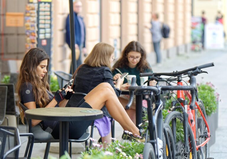 Mujeres sentadas en una terraza, una revisando su teléfono móvil.