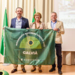 Tres personas sosteniendo una bandera del Movimiento Banderas Verdes 2025 en un evento.