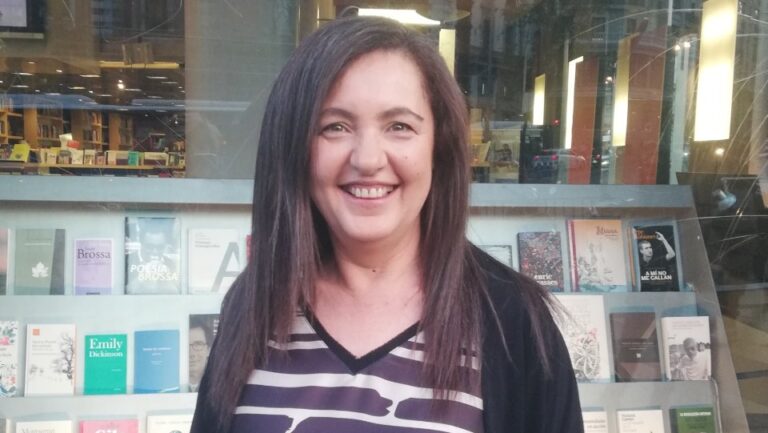Mujer sonriendo frente a una librería, participando en evento sobre liderazgo femenino.