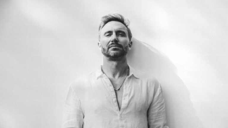 David Guetta posando con una camisa blanca en un fondo claro