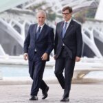 Dos hombres caminando junto a una estructura moderna en un entorno urbano.
