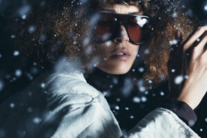 Modelo con abrigo blanco y gafas en un entorno nevado
