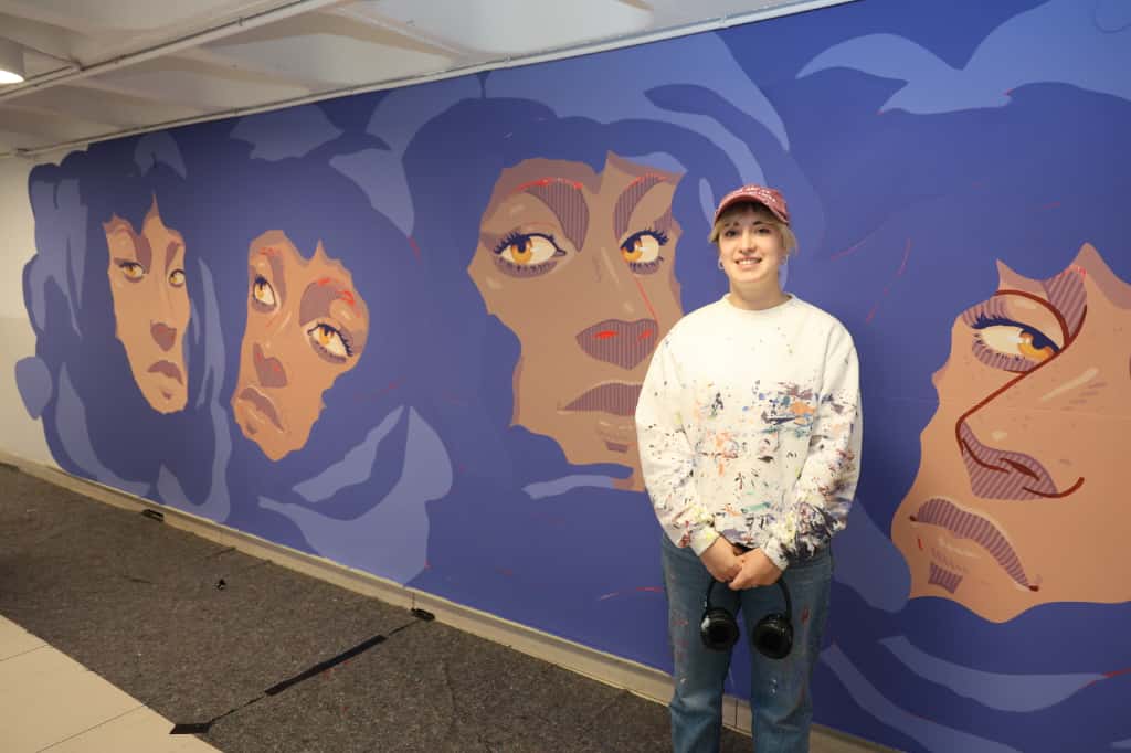 Muralista sonriente junto a su obra en el evento Let’s Art 2025.